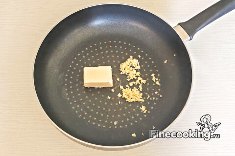 Сливочное масло в сковороде и измельчённый чеснок.