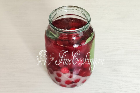 Банка с вишней, сахаром и вишнёвыми листьями, залитая водкой.